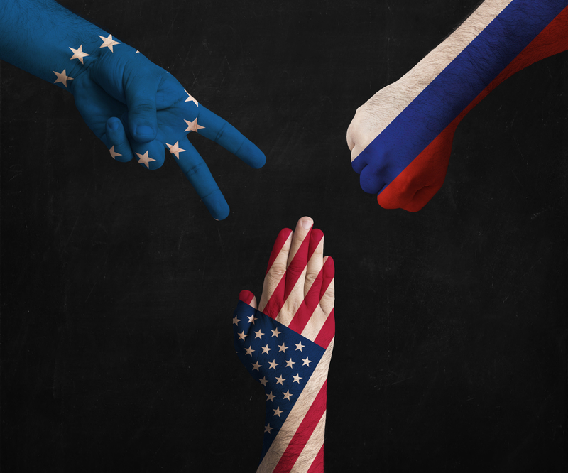 hands decorated in flags of EU, USA and Russia showing Scissors, paper, stone - symbolizing the political games between them